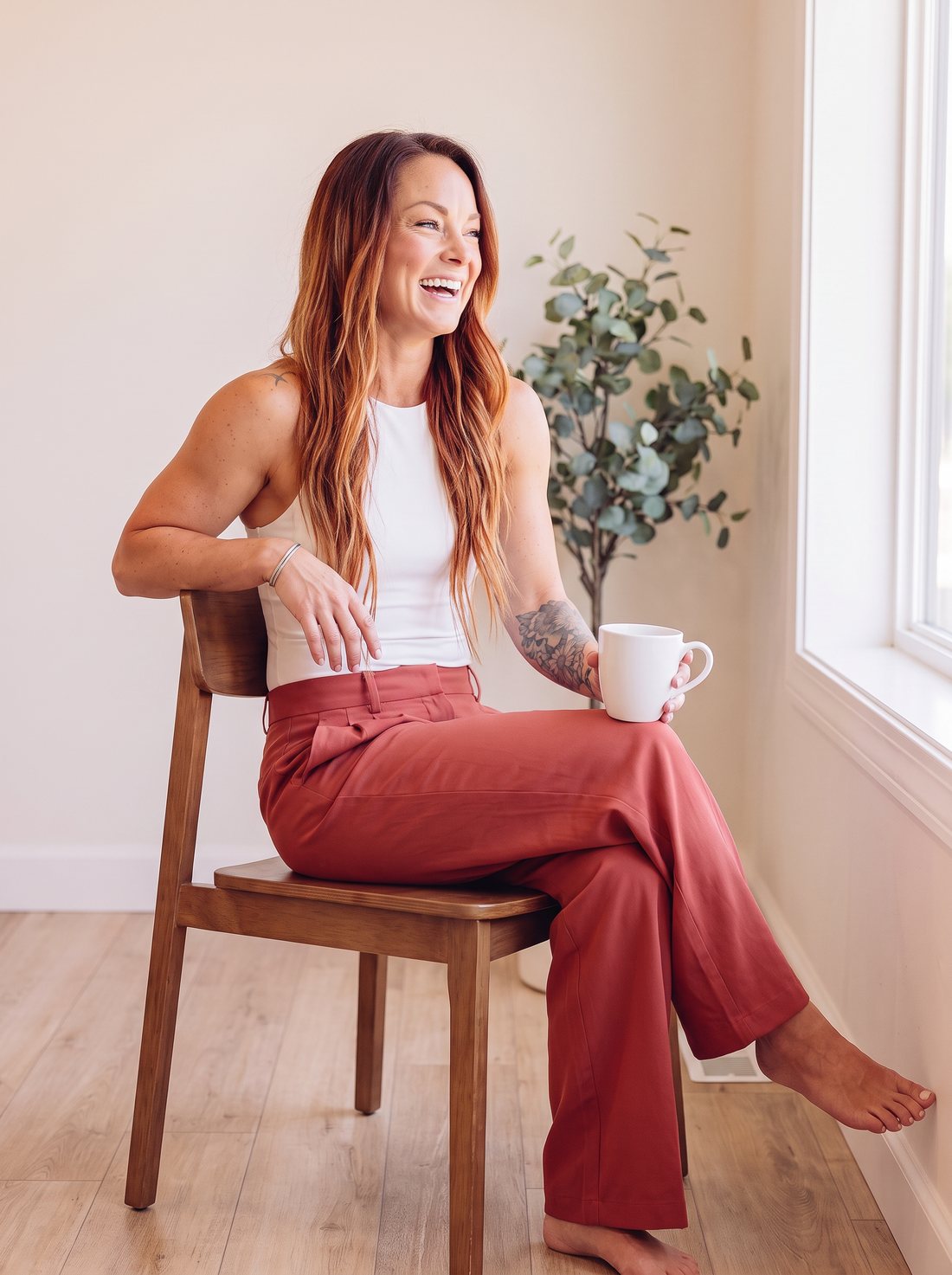 Ashley laughing on a wooden chair with a coffee mug