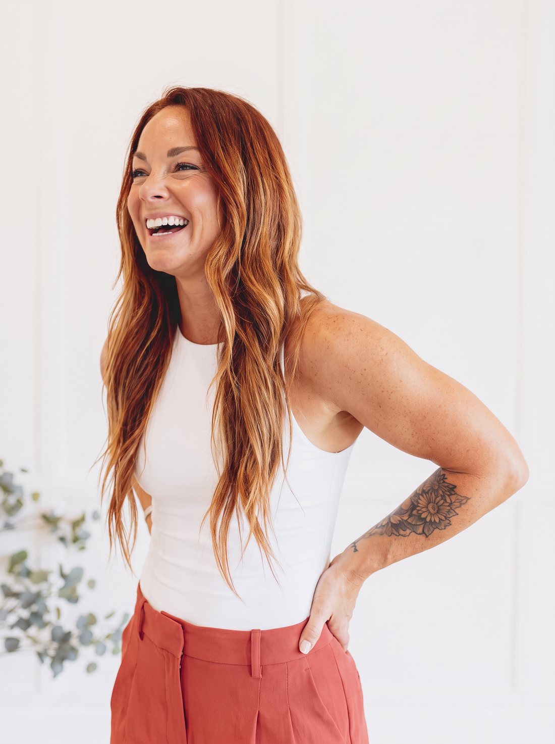 Ashley laughing in a white tank and rust trousers