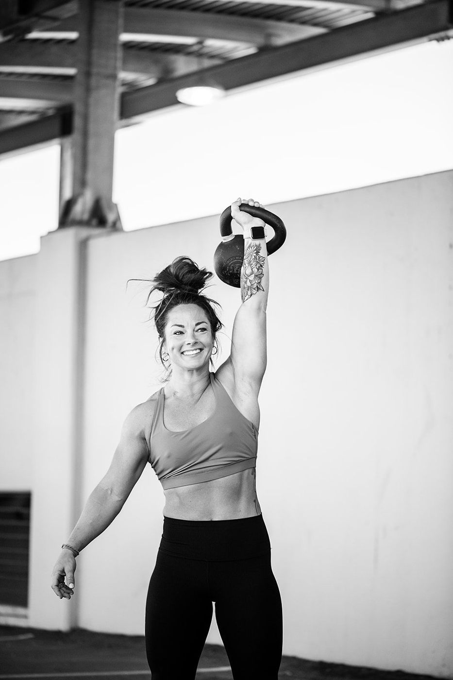 Ashley smiling with a kettlebell overhead, black and white